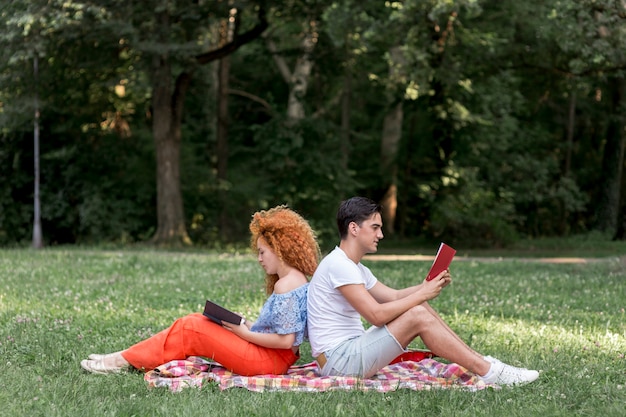 Feliz pareja de jóvenes sentados espalda con espalda en una manta de picnic