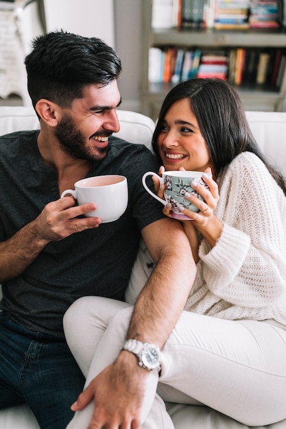 Feliz pareja de jóvenes sentados en el sofá disfrutando del café