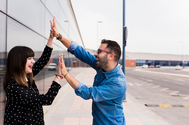 Feliz pareja de jóvenes tocando las palmas de los demás en la calle