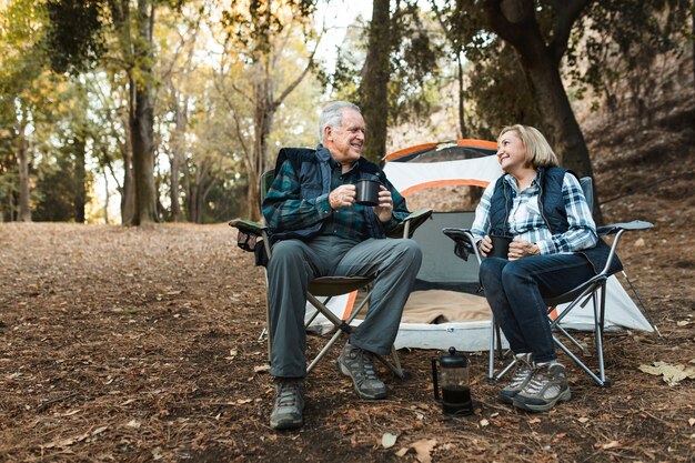 Feliz pareja de jubilados tomando un café junto a la carpa en el bosque