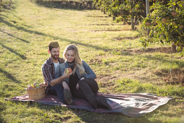 Feliz pareja juntos sentados sobre una manta en huerto de manzanas