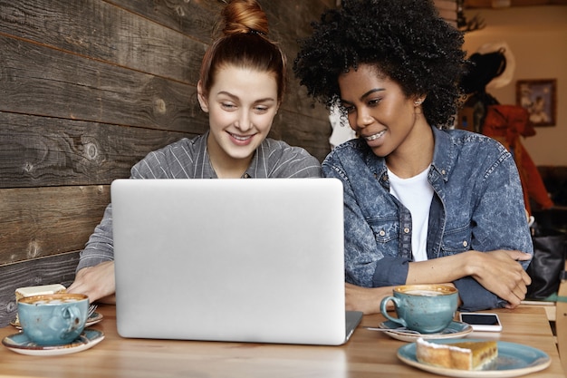 Feliz pareja de lesbianas interracial alegre disfrutando de la comunicación en línea en la computadora portátil
