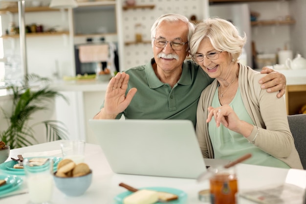 Feliz pareja madura haciendo videollamadas a través de una laptop en casa