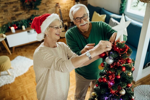 Feliz pareja madura preparándose para Navidad y decorando el árbol en casa