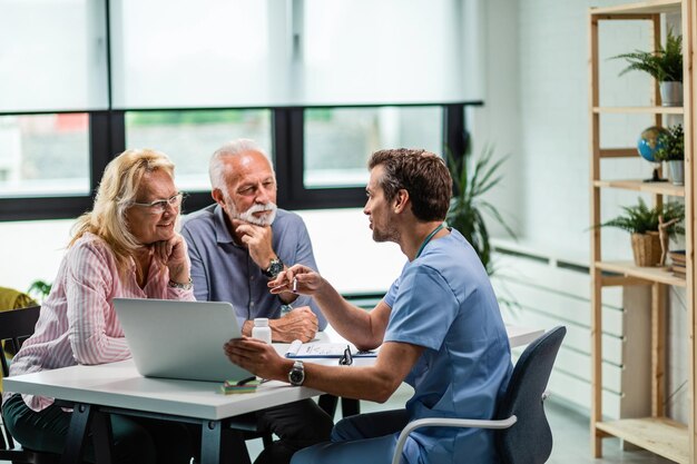 Feliz pareja madura y su médico comunicándose mientras usan una computadora portátil durante una cita médica