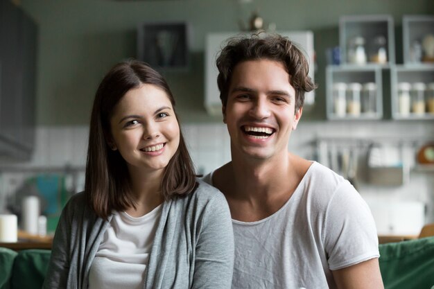 Feliz pareja milenaria mirando a la cámara en la cocina, retrato en la cabeza