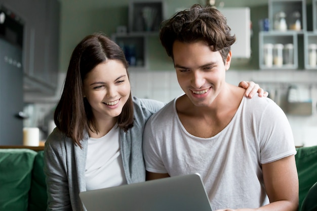 Feliz pareja milenaria sonriendo mirando la pantalla del portátil haciendo videollamada