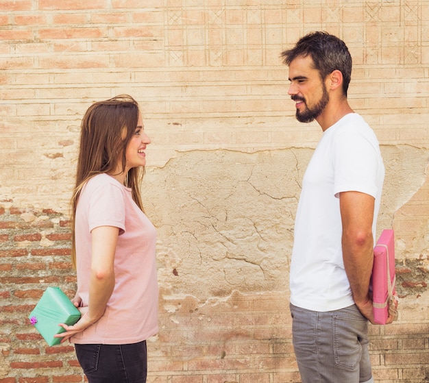 Foto gratuita feliz pareja mirando el uno al otro escondiendo el regalo detrás