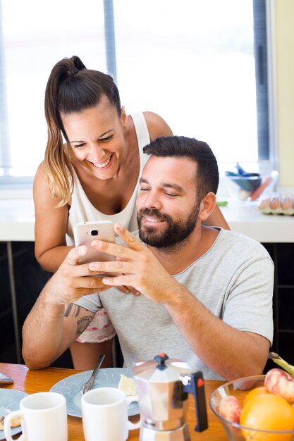 Feliz pareja mirando la pantalla del teléfono móvil en el desayuno