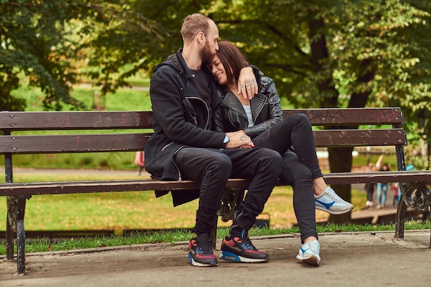 Feliz pareja moderna abrazándose en un banco en el parque. Disfrutando de su amor y la naturaleza.