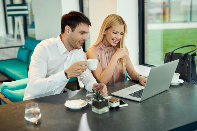 Feliz pareja de negocios usando computadora mientras bebe café en un café El foco está en la mujer