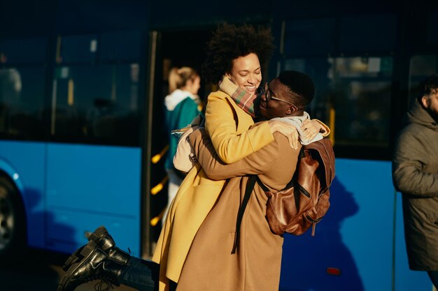 Feliz pareja negra divirtiéndose y abrazándose mientras se reunían en la estación de autobuses