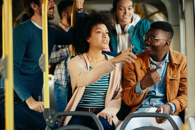 Feliz pareja negra hablando y señalando por la ventana mientras viaja en autobús