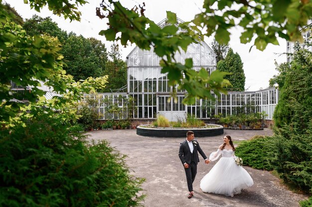 Feliz pareja de novios caminando en el jardín mirándose con amor hermosa chica con un vestido hinchado con un hombre con traje elegante Momento de ternura pareja amorosa