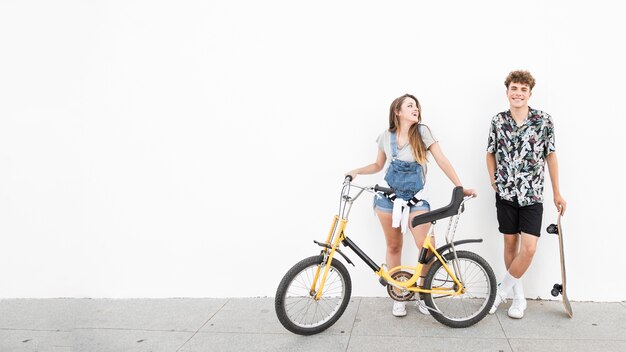 Foto gratuita feliz pareja de pie con bicicleta y patineta en la acera