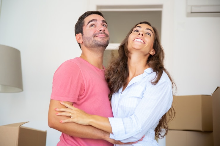 Foto gratuito feliz pareja de pie entre cajas de cartón y abrazándose, mirando su nuevo apartamento