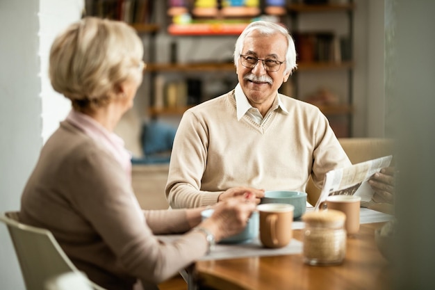 Feliz pareja senior hablando mientras desayuna en la mesa de comedor El foco está en el hombre