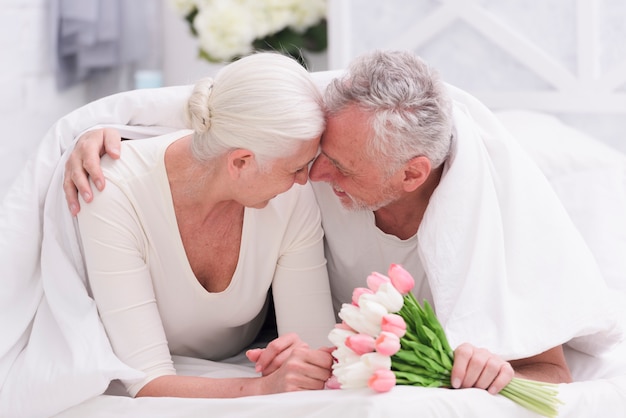 Feliz pareja senior romántica en la cama con flores de tulipán en la mano