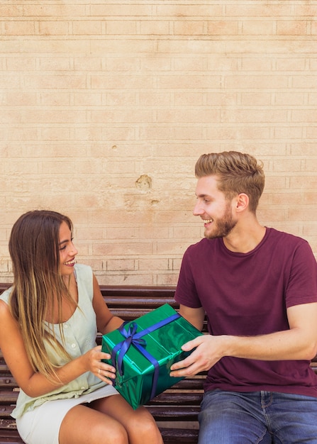 Foto gratuita feliz pareja sentada en el banco con presente