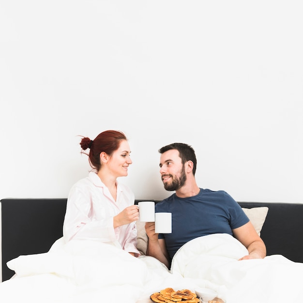 Foto gratuita feliz pareja sentada en la cama bebiendo café