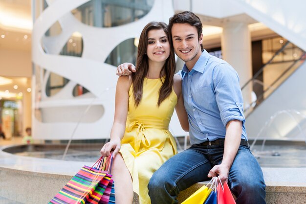 Feliz pareja sentada en el centro comercial junto a la fuente