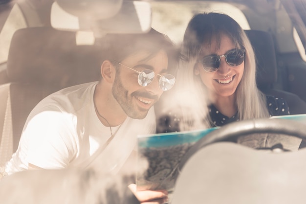 Feliz pareja sentada en el coche mirando el mapa