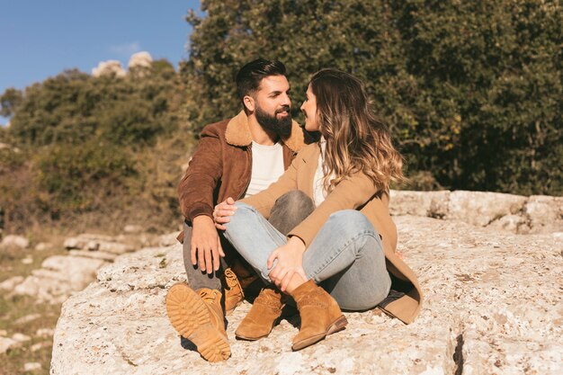 Feliz pareja sentada en una roca y mirándose