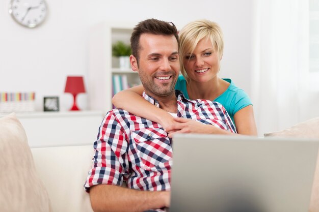 Feliz pareja sentada en la sala de estar y usando laptop