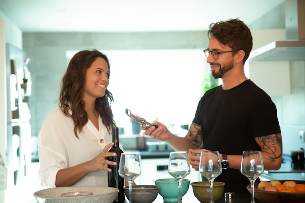 Feliz pareja sirviendo la cena y abriendo una botella de vino