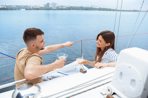 Feliz pareja sonriente bebiendo cócteles de vodka en fiesta en barco al aire libre, alegre y feliz.