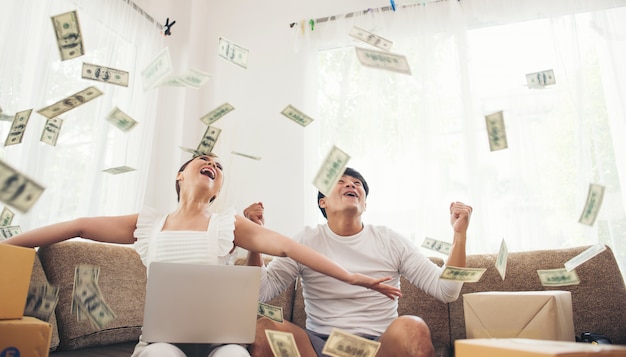 Feliz pareja sonriente exitosa sentado bajo la lluvia de dinero. Concepto de negocio en linea