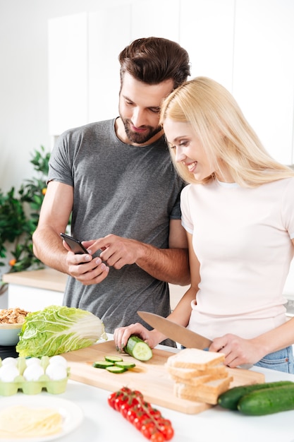 Feliz pareja sonriente con teléfono móvil para encontrar una receta