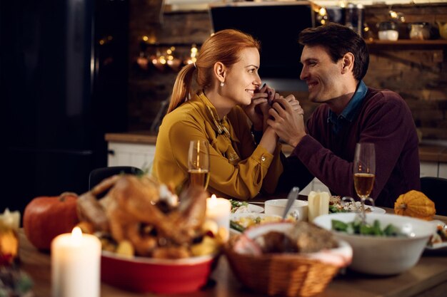 Feliz pareja tomados de la mano y hablando durante la comida de Acción de Gracias en el comedor