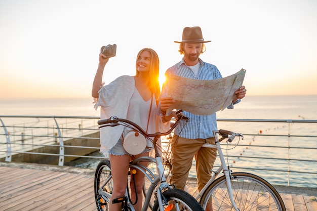 Feliz pareja viajando en verano en bicicleta, mirando en el mapa haciendo turismo y tomando fotos