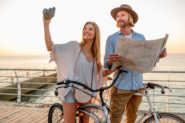 Feliz pareja viajando en verano en bicicleta, mirando en el mapa haciendo turismo y tomando fotos