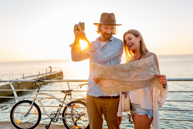 Feliz pareja viajando en verano en bicicleta, mirando un mapa y tomando fotos con la cámara