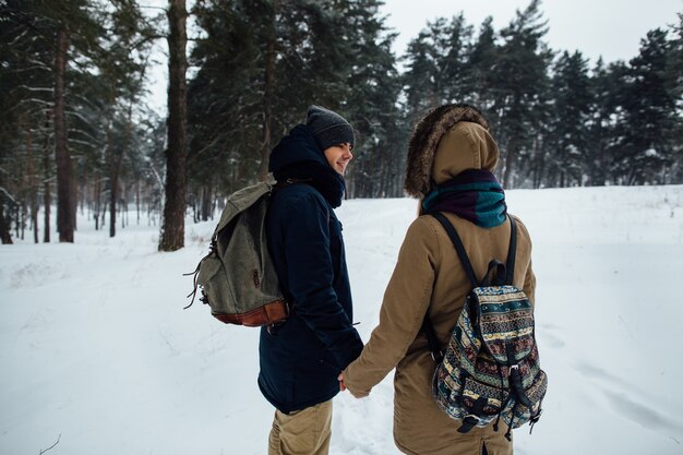 Feliz pareja de viajeros tomados de la mano en el bosque de invierno cubierto de nieve