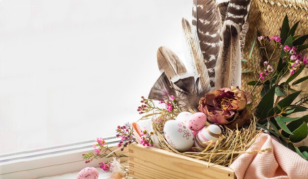 Feliz Pascua de fondo. Huevos de Pascua rosados en un nido con adornos florales y plumas cerca de la ventana