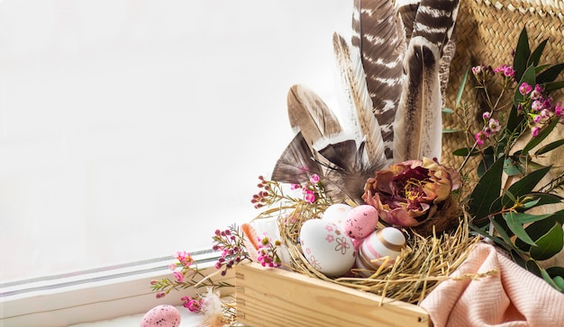 Feliz Pascua de fondo. Huevos de Pascua rosados en un nido con adornos florales y plumas cerca de la ventana