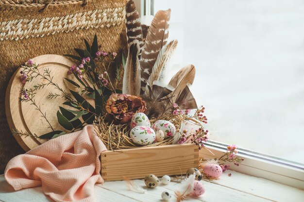 Feliz Pascua de fondo. Huevos de Pascua rosados en un nido con adornos florales y plumas cerca de la ventana