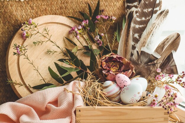 Feliz Pascua de fondo. Huevos de Pascua rosados en un nido con adornos florales y plumas cerca de la ventana