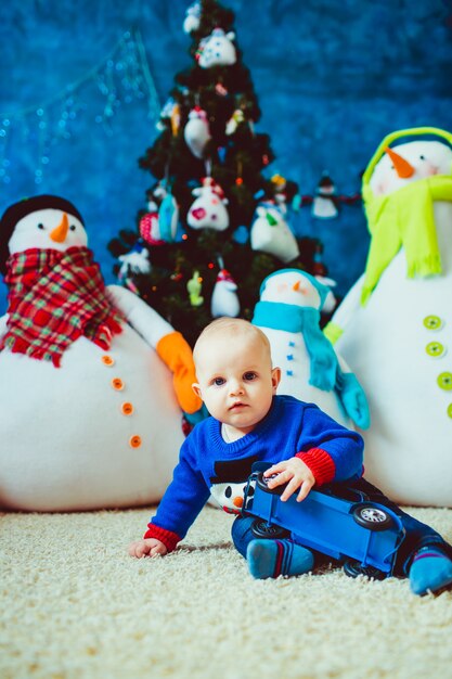 feliz poco niño cerca de muñeco de nieve de juguete en el estudio