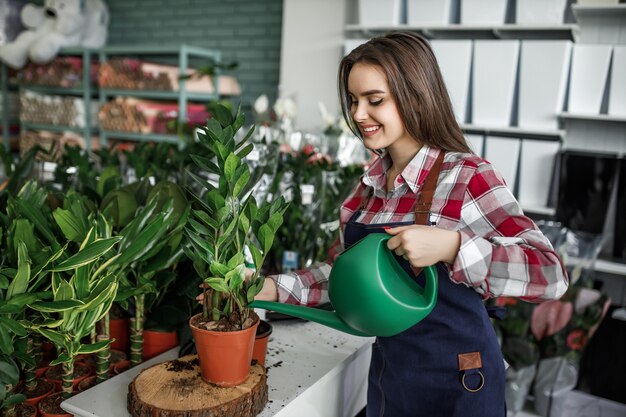 Feliz y positiva joven trabajando en invernadero y disfrutando de regar hermosas flores