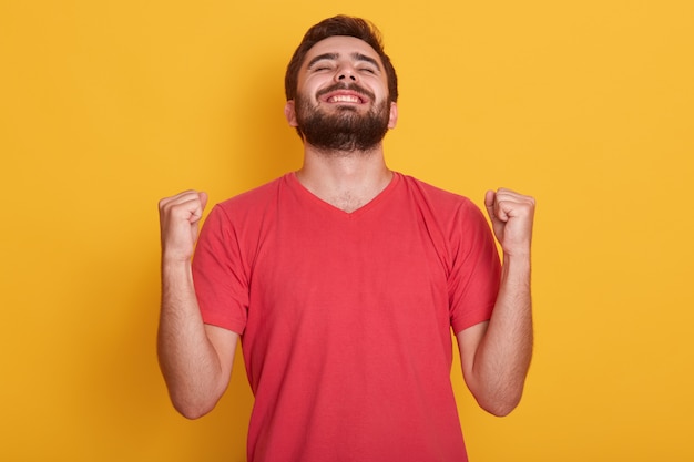 feliz positivo emocionado joven apretando los puños y gritando, vistiendo una camiseta roja casual, teniendo buenas noticias, celebrando su victoria o éxito, gana la lotería. Concepto de emociones de las personas.