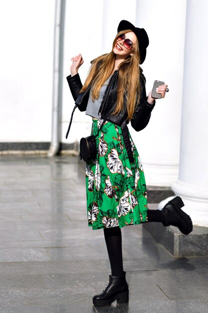 Feliz primavera soleada de una mujer joven y bonita con cabello largo morena con sombrero, falda verde larga, tacones caminando en la calle. Modelo de moda, expresando emociones positivas a la cámara, sonriendo, alegría