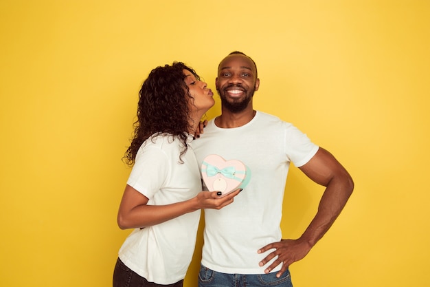 Feliz de recibir un regalo. celebración del día de san valentín, feliz pareja afroamericana aislada sobre fondo amarillo de estudio. concepto de emociones humanas, expresión facial, amor, relaciones, vacaciones románticas.