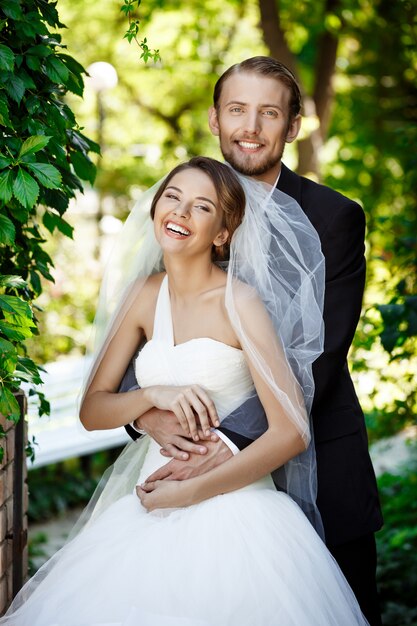 Feliz recién casados sonriendo, abrazándose, posando en el parque.