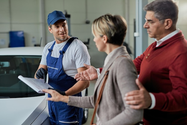 Feliz reparador de automóviles y pareja analizando datos mientras se comunica en un taller