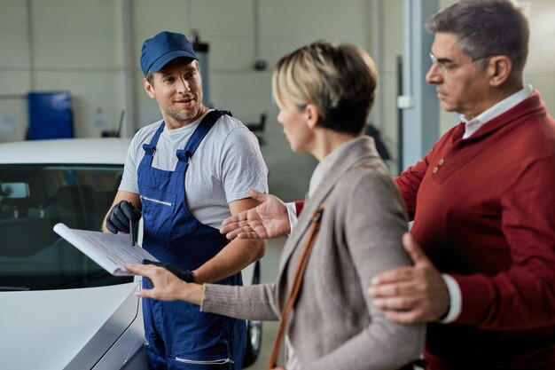 Feliz reparador de automóviles y pareja analizando datos mientras se comunica en un taller