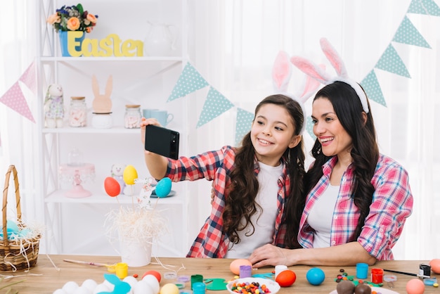 Feliz retrato de madre e hija tomando autorretrato en celular en el día de Pascua